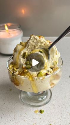 an ice cream sundae with pistachio topping and a candle in the background