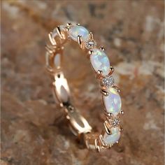 a white opal and diamond ring sitting on top of a rock