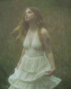 a woman in a white dress walking through tall grass