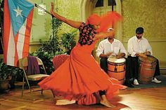 a woman in an orange dress is dancing with two men behind her and one man sitting on the floor