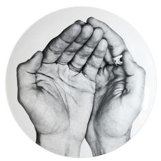 two hands on a white plate with black and white ink art work in the middle