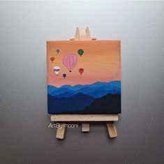 an easel with a painting on it that has hot air balloons in the sky