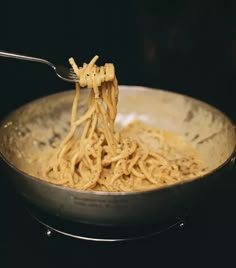 a fork full of noodles being lifted from a skillet with noodle in it