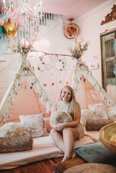 a woman sitting on top of a bed holding a teddy bear in front of a teepee