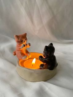 two cats sitting in a bowl with a lit candle