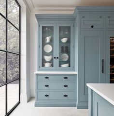 an empty kitchen with blue cabinets and white counter tops, in front of a large window