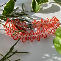 two red bracelets sitting on top of a table next to green leaves and plants