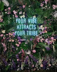 a neon sign that says your vibe attracts your tribe surrounded by flowers and plants in the background