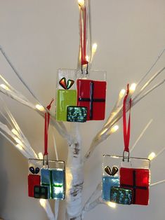 three christmas ornaments hanging from a tree with white branches and lights on the branches are wrapped in red ribbon