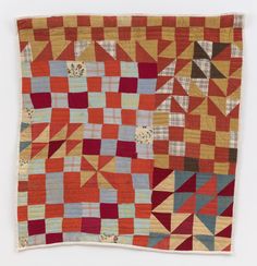 an orange and red patchwork quilt hanging on a wall in front of a white background