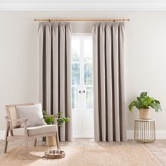 a living room with a chair, rug and window covered in grey drapes next to a potted plant