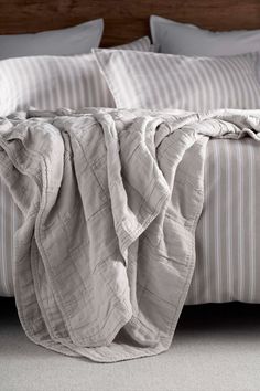 an unmade bed with white and gray striped linens on the headboard, along with two pillows