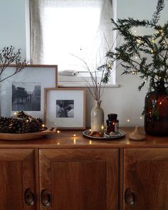 there is a wooden cabinet with candles and pictures on the top, along with pine cones