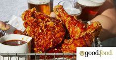 a basket filled with fried chicken next to two mugs of beer