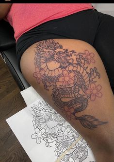 a woman with a dragon tattoo on her thigh next to a piece of art paper