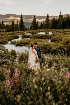 a bride and groom standing in the middle of a field with mountains in the background