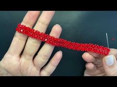 two hands are holding something red and one has a needle in the middle with beads on it