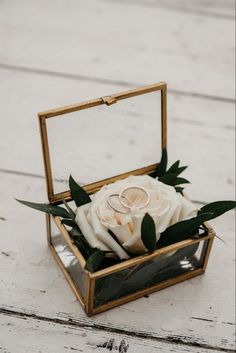 two wedding rings are placed in a box with greenery on the table next to it