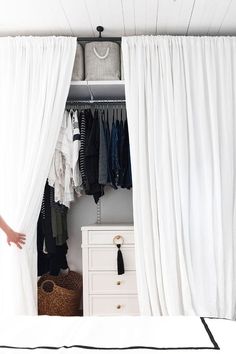 an open closet with white curtains and clothes