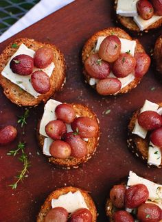 small crackers topped with grapes and cheese on top of a wooden table next to other snacks