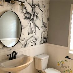 a white toilet sitting next to a sink in a bathroom under a mirror with flowers on it