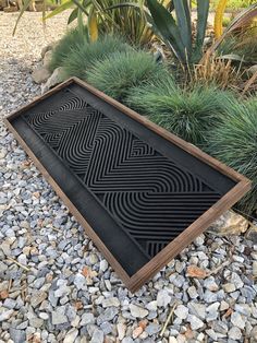 a black and brown floor mat sitting on top of gravel next to some plants in a garden