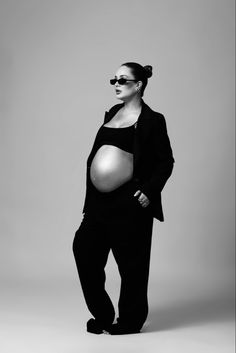 a pregnant woman wearing sunglasses poses for a black and white photo with her belly exposed