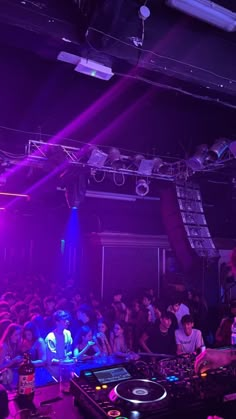 a dj mixing in front of a large crowd at a nightclub with purple lighting and people watching