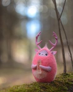 a pink stuffed animal sitting on top of a moss covered ground next to a tree