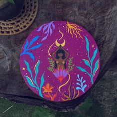 a painted plate sitting on top of a tree stump next to a basket and potted plant