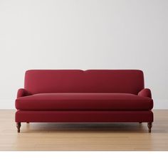 a red couch sitting on top of a hard wood floor next to a white wall