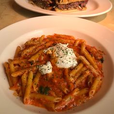 two plates of pasta with meat and sauce on them, one has a sandwich in the background