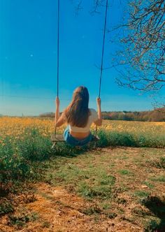 a woman is sitting on a swing in the middle of a field with yellow flowers