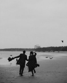 black and white photograph of two people walking on the beach with kites in the sky