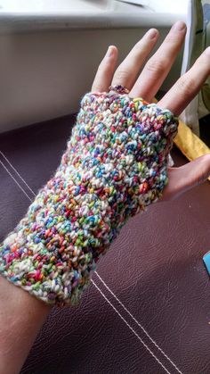 a person wearing a colorful knitted armwarf on their left hand, next to a book