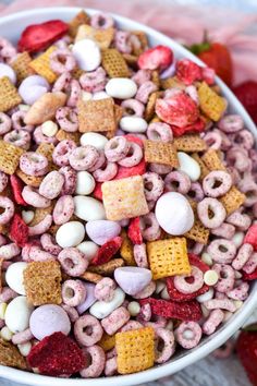 a bowl filled with cereal and marshmallows on top of a table next to strawberries