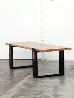 a wooden table sitting on top of a cement floor next to a white wall and black metal frame