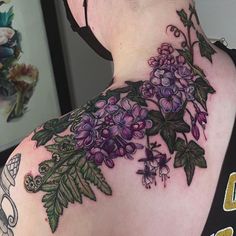 the back of a woman's shoulder with flowers and leaves tattooed on her upper arm