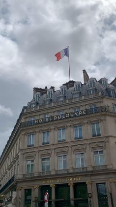 a tall building with a flag on top of it's roof in front of a cloudy sky