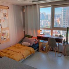 a bedroom with a bed, desk and window overlooking the cityscape in the distance