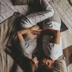 a man and woman laying on top of a bed next to each other with their arms around each other