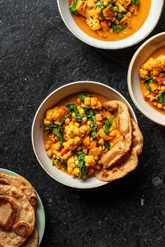 three bowls filled with food sitting on top of a table next to some pita bread