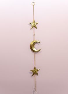 three gold stars and a crescent hanging from a chain on a pink wall with a white background