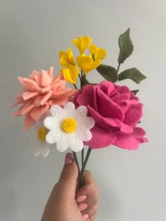 a person holding three flowers in their hand with white and yellow flowers on the top