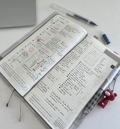 an open notebook sitting on top of a white table next to a laptop and pen