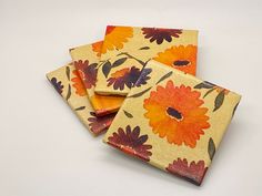 four square coasters with orange and red flowers on yellow fabric, set against a white background