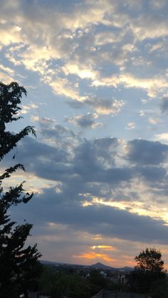 the sun is setting behind some clouds in the sky over houses and trees on a hill