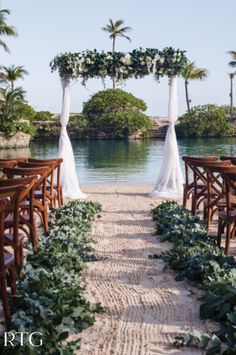 an outdoor wedding setup with white draping and greenery on the ground next to water