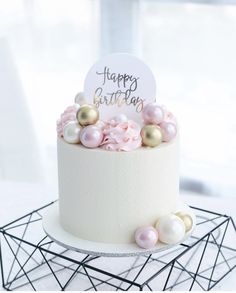 a white cake with pink and gold decorations on top is sitting on a black wire stand