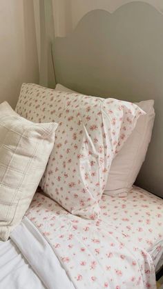 a bed with white sheets and pink flowers on the pillowcase, next to a window